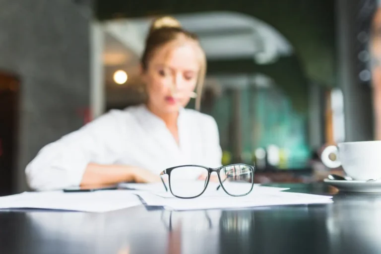 Devojka u kafiću drži naočare na stolu.